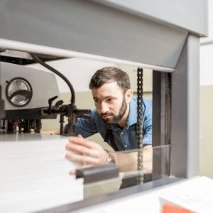 Man working with paper sheets feeling into the printing machine at the manufacturing